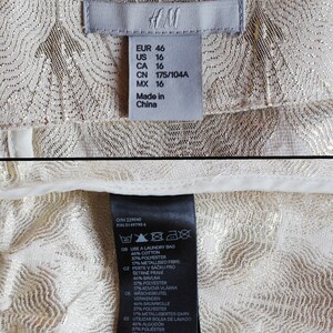 May include: A white tag with black text detailing the size and care instructions for a garment. The tag reads "EUR 46, US 16, CA 16, CN 175/104A, MX 16, Made in China". The care instructions include "Use a laundry bag, 46% cotton, 37% polyester, 17% metallised fibre".