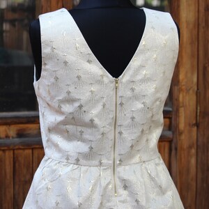 May include: A white sleeveless top with a gold metallic pattern and a zipper down the back. The top has a peplum hem.