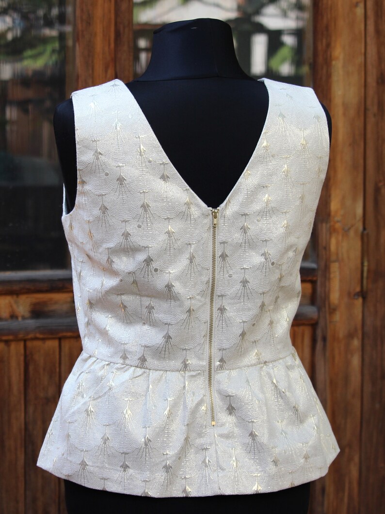 May include: A white sleeveless top with a gold metallic pattern and a zipper down the back. The top has a peplum hem.
