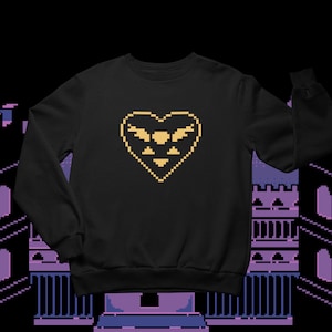 Puede incluir: Sudadera negra con un diseño de corazón pixelado amarillo con un símbolo alado en su interior. El corazón es un símbolo común en los videojuegos.