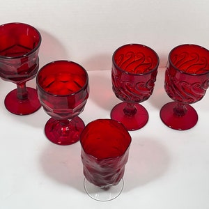 May include: A collection of five ruby red goblets. The glasses feature various designs, including geometric patterns and swirling textures. The goblets have a stem and a round base. The glassware is suitable for serving beverages.