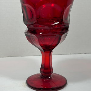 May include: A ruby red glass goblet with a textured, geometric design. The stem and base are solid red, and the bowl has a series of rounded, raised patterns. The glass has a high-gloss finish.
