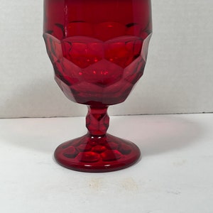 May include: A ruby red goblet with a faceted design. The glass has a stem and a round base. The goblet is made of glass and is suitable for serving beverages. The glass is empty.