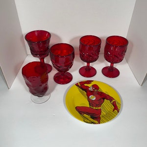 May include: A collection of red glassware and a yellow plate featuring The Flash. The glassware includes five wine glasses with varying designs. The plate has a red and yellow color scheme with a graphic of The Flash.