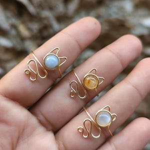 Puede incluir: Tres anillos de alambre dorado con piedras de diferentes colores. Los anillos tienen forma de cabeza de gato con una cola enroscada.