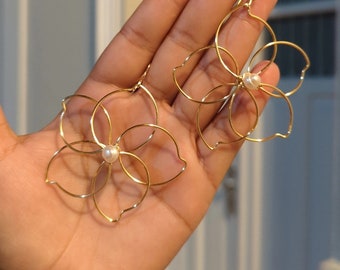 May include: A pair of gold flower-shaped earrings with a pearl in the center of each flower.