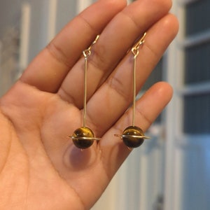 A r e t e s  d e  s a t u r n o🪐
-Aretes largos de planeta (Saturno) hechos con alambre de chapa de oro (14k) y ojos de tigre de 10 mm
Miden aprox. 8 cm