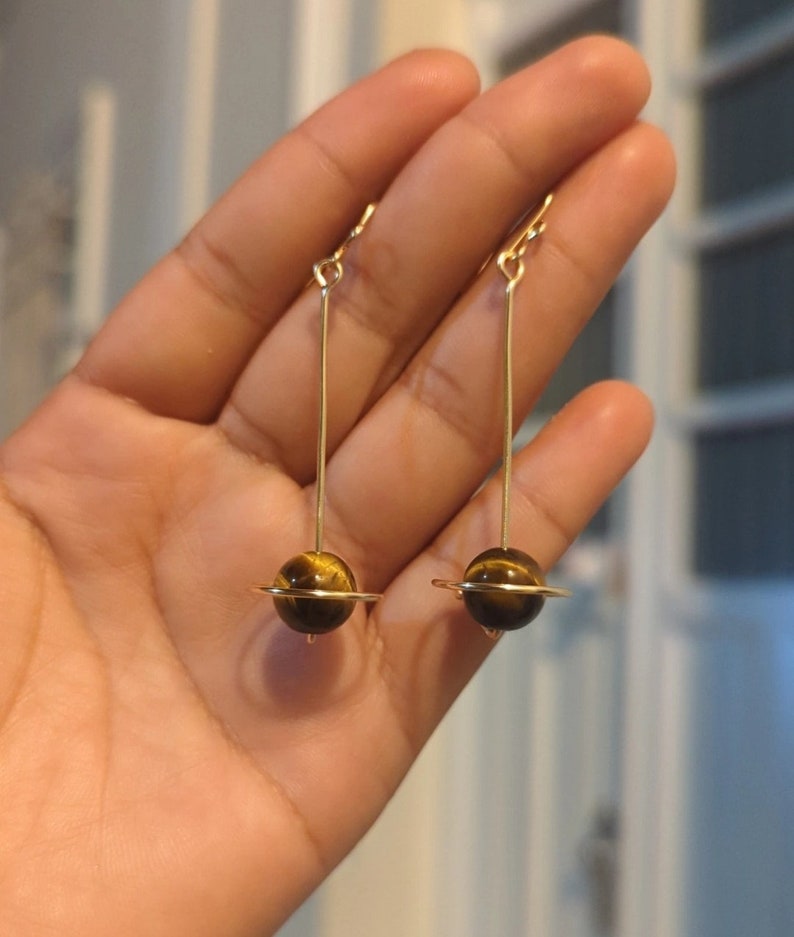 A r e t e s  d e  s a t u r n o🪐
-Aretes largos de planeta (Saturno) hechos con alambre de chapa de oro (14k) y ojos de tigre de 10 mm
Miden aprox. 8 cm