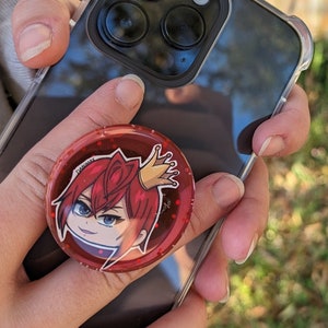Könnte beinhalten: Ein roter und goldener Handy-Griff mit einer Comicfigur mit roten Haaren, die eine goldene Krone trägt. Der Griff ist an einem schwarzen Handy-Case befestigt.