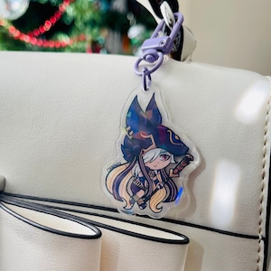 May include: A white handbag with a black trim and a clear keychain featuring a cartoon character with long blonde hair, a black hat, and a staff. The character is wearing a purple and black outfit.