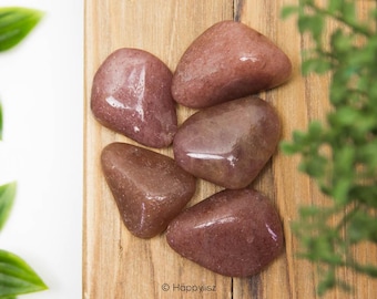 May include: Five smooth, heart-shaped rose quartz stones in shades of pink and brown, arranged on a wooden surface.
