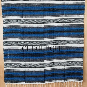 May include: A blue and white striped Mexican blanket with black accents and fringe. The blanket is made of woven fabric and has a traditional design.