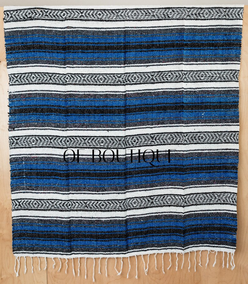 May include: A blue and white striped Mexican blanket with black accents and fringe. The blanket is made of woven fabric and has a traditional design.