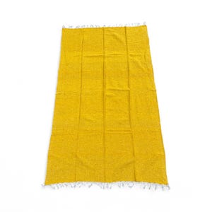 May include: A rectangular, yellow woven blanket with a textured surface. The blanket has a fringe detail along the short edges. The blanket is displayed on a white background.