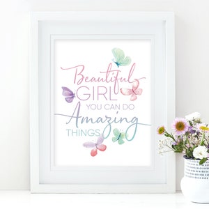 May include: A framed print with the words "Beautiful Girl You Can Do Amazing Things" in a script font, with watercolor butterflies in shades of pink, purple, and teal. The print is in a white frame.