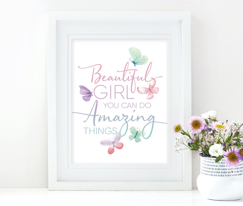 May include: A framed print with the words "Beautiful Girl You Can Do Amazing Things" in a script font, with watercolor butterflies in shades of pink, purple, and teal. The print is in a white frame.