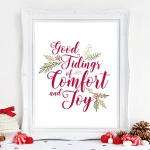 Może przedstawiać: Biały wydruk w ramie z tekstem "Good Tidings of Comfort and Joy" w czerwonym, ozdobnym piśmie z zielonymi liśćmi i czerwonymi jagodami.