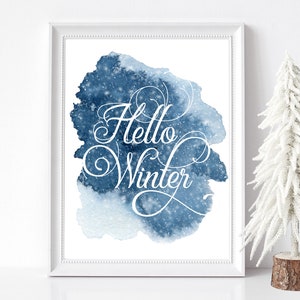 Może przedstawiać: Biały wydruk w ramie z niebieskim tłem akwarelowym i tekstem "Hello Winter" w białym, ozdobnym piśmie.