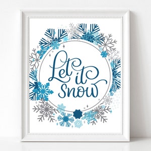 May include: A white framed print with a blue and grey snowflake wreath surrounding a circle with the text "Let it snow" in blue cursive lettering.