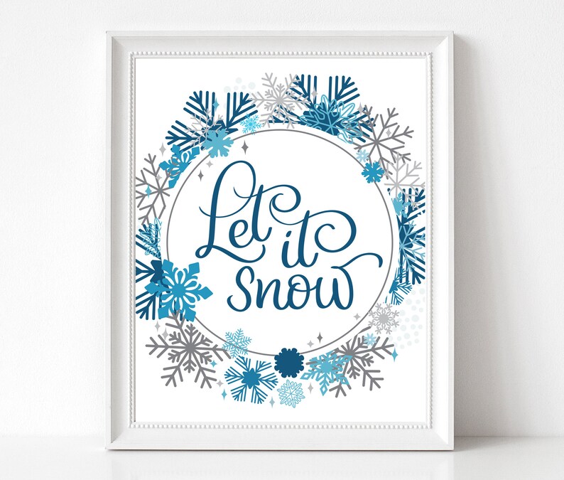 May include: A white framed print with a blue and grey snowflake wreath surrounding a circle with the text "Let it snow" in blue cursive lettering.