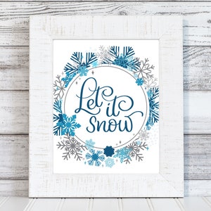 May include: White framed print featuring a blue and grey snowflake wreath with the text "Let it snow" in a blue cursive font.