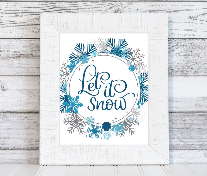 May include: White framed print featuring a blue and grey snowflake wreath with the text "Let it snow" in a blue cursive font.