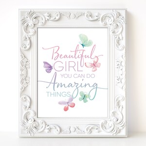 May include: A framed print with the words "Beautiful Girl You Can Do Amazing Things" in a script font. The print features watercolor butterflies in shades of pink, purple, and teal. The frame is white with ornate detailing.