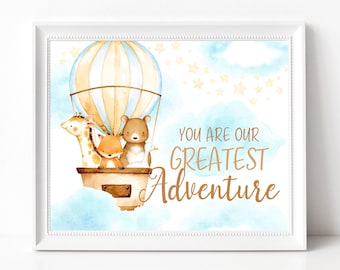 May include: A watercolor illustration of a hot air balloon with a giraffe, fox, bear, and bird inside. The balloon is floating in a blue sky with white clouds and gold stars. The text "You are our greatest adventure" is written in gold lettering.