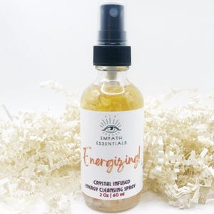 May include: A clear glass spray bottle with a black cap and a white label. The label reads "Empath Essentials Energizing! Crystal Infused Energy Cleansing Spray 2 oz | 60 ml". The bottle contains a yellow liquid.