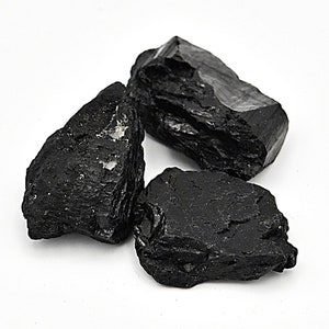 May include: Three black tumbled stones of black tourmaline, a dark, opaque gemstone.