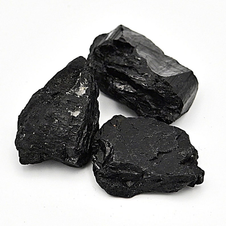 May include: Three black tumbled stones of black tourmaline, a dark, opaque gemstone.