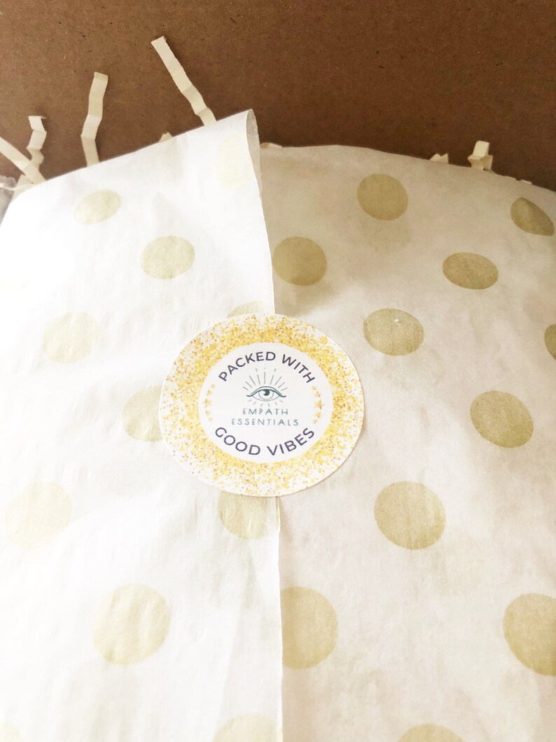 May include: A white paper bag with gold polka dots and a sticker that says "Packed with Empath Essentials Good Vibes". The sticker has a gold glitter background and a blue eye symbol.
