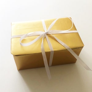 May include: A gold gift box with a white satin ribbon tied in a bow.