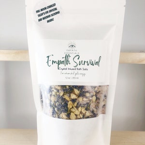 May include: White pouch with a clear window showing crystal infused bath salts. The pouch has a label that reads "Empath Essentials Empath Survival Crystal Infused Bath Salts For when shit gets crazy 12 oz | 355 ml".