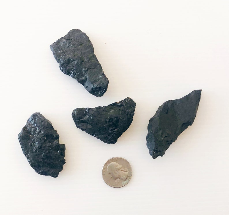 May include: Four black, irregularly shaped, rough-textured stones, with one stone slightly larger than the others. A silver US quarter is included for size comparison.