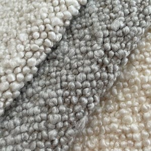 May include: Close-up of three different types of textured fabric. The fabric is a light gray, a medium gray, and a white. The fabric is made of small, round loops.