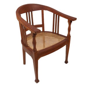 May include: A wooden armchair with a curved back and armrests. The chair features a woven cane seat and a warm brown finish. The design includes vertical back supports and decorative turned details on the armrest supports.