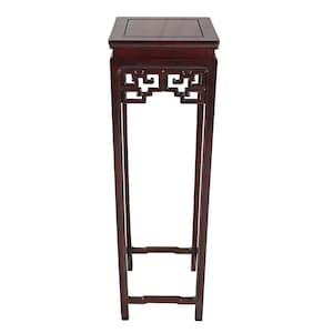 May include: A tall, dark wood plant stand with a square top and decorative openwork design. The stand has a slender, rectangular frame and is finished in a rich, reddish-brown hue. The stand is designed to display plants or decorative items.