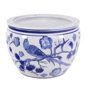 May include: A white ceramic planter with a blue bird and floral design. The planter has a wide, round shape with a detailed rim and is decorated with blue flowers and a bird perched on a branch.