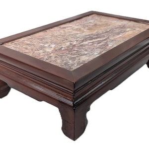 May include: A rectangular display stand featuring a dark brown wooden frame with four curved legs and a smooth, polished stone inlay top. The stone surface displays a marbled pattern with swirling shades of beige, brown, and cream colors.