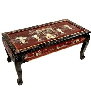May include: A red and black lacquered coffee table with intricate inlaid mother-of-pearl designs depicting a Chinese garden scene. The table has four carved legs and a rectangular top.