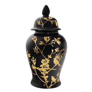 May include: A black ceramic ginger jar with a lid, adorned with gold floral and bird designs. The jar has a rounded body and a conical finial on the lid. The gold detailing creates a striking contrast against the black background.