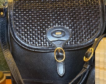 Peut inclure: Sac bandoulière en cuir noir avec rabat tressé et détails dorés. Le sac est de forme rectangulaire avec une fermeture à rabat sécurisée par une boucle dorée. La bandoulière est réglable.