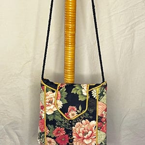 May include: A black fabric crossbody bag with a floral print and gold trim. The bag has a long black strap and a flap closure.