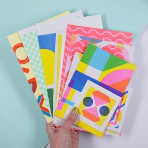 May include: A collection of rectangular paper cards featuring vibrant geometric patterns in neon pink, bright yellow, lime green, and blue. The designs include checkered grids, solid circles, and abstract shapes printed on white cardstock paper.