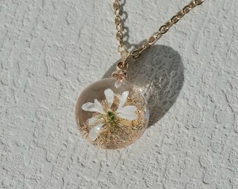 May include: A gold chain necklace with a clear glass pendant containing a delicate white flower.
