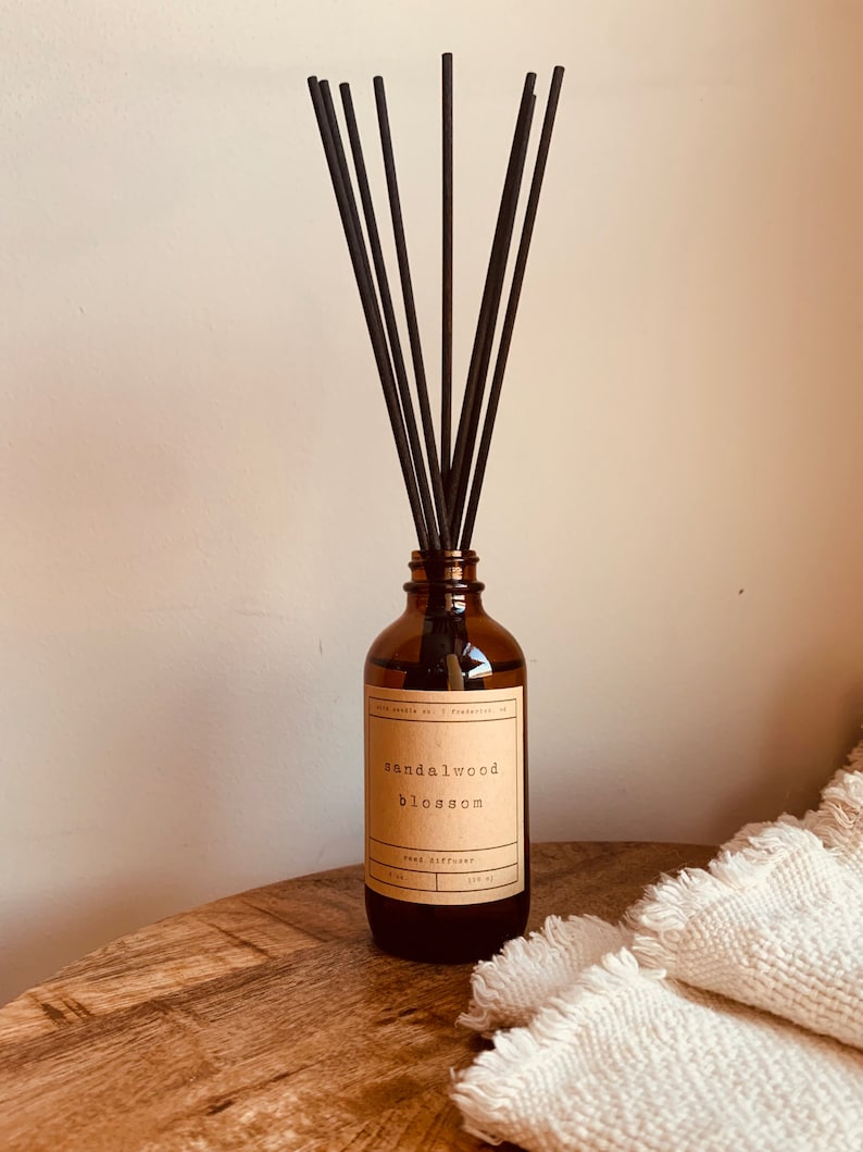 May include: A brown glass bottle with black reeds and a label that reads "sandalwood blossom reed diffuser".