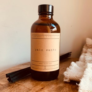 May include: A brown glass bottle with a black lid and a brown paper label that reads "palo santo reed diffuser 4 oz. 118 ml".