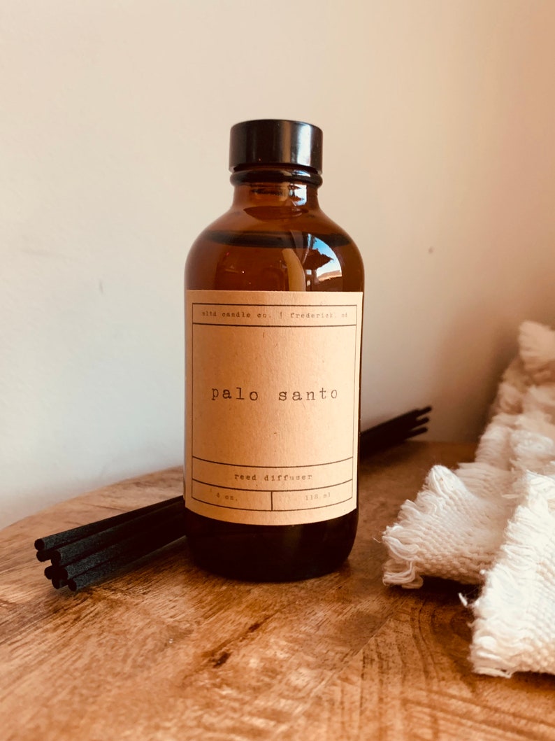 May include: A brown glass bottle with a black lid and a brown paper label that reads "palo santo reed diffuser 4 oz. 118 ml".