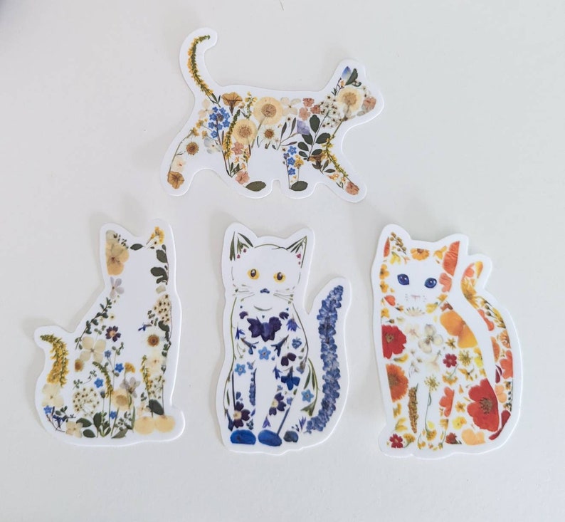 May include: Four cat stickers with a floral design. Each cat is a different color and has a different floral pattern. The cats are all in a sitting position.
